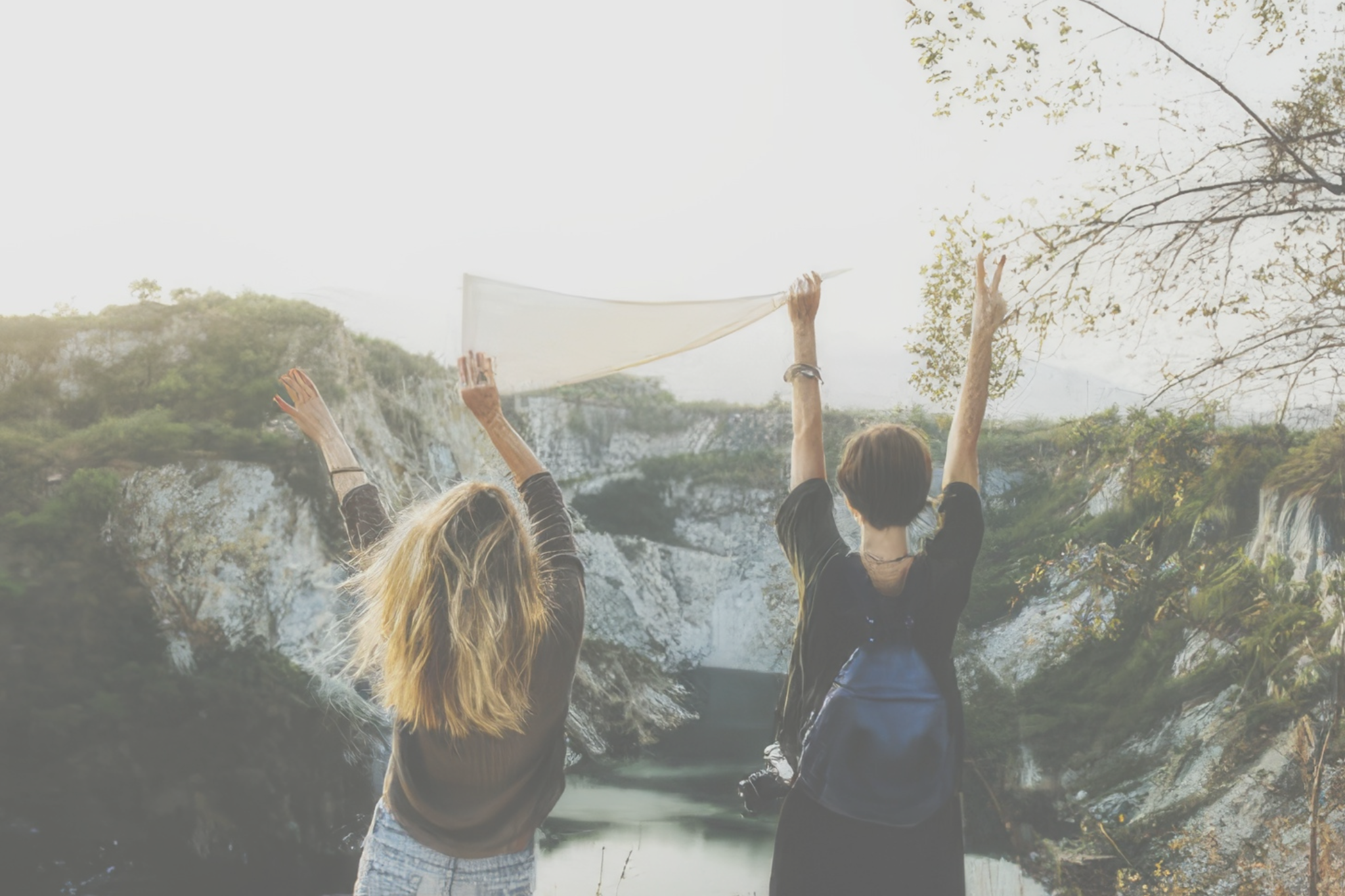 Two young women holding a flag at the top of a mountain