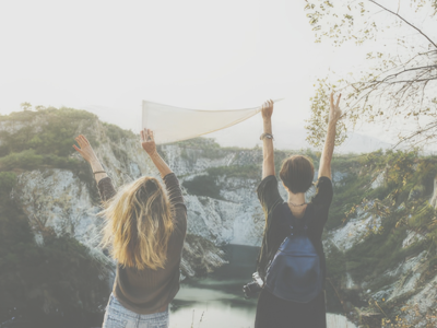 Two young women holding a flag at the top of a mountain
