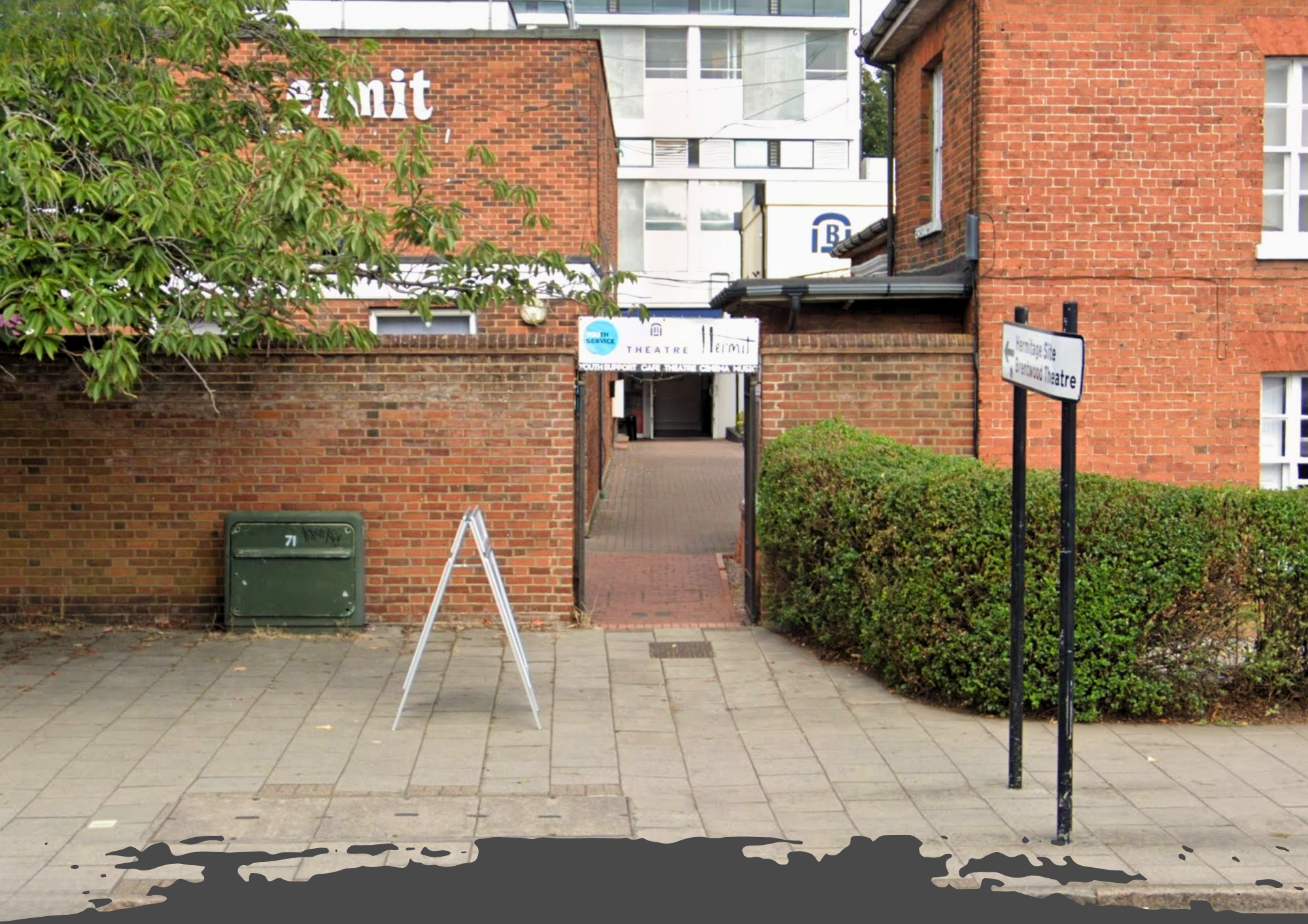Entrance to Brentwood Youth Centre through a brick-walled passage, with signs for ‘Hermit Theatre’ and ‘Youth Service’ visible, surrounded by greenery.