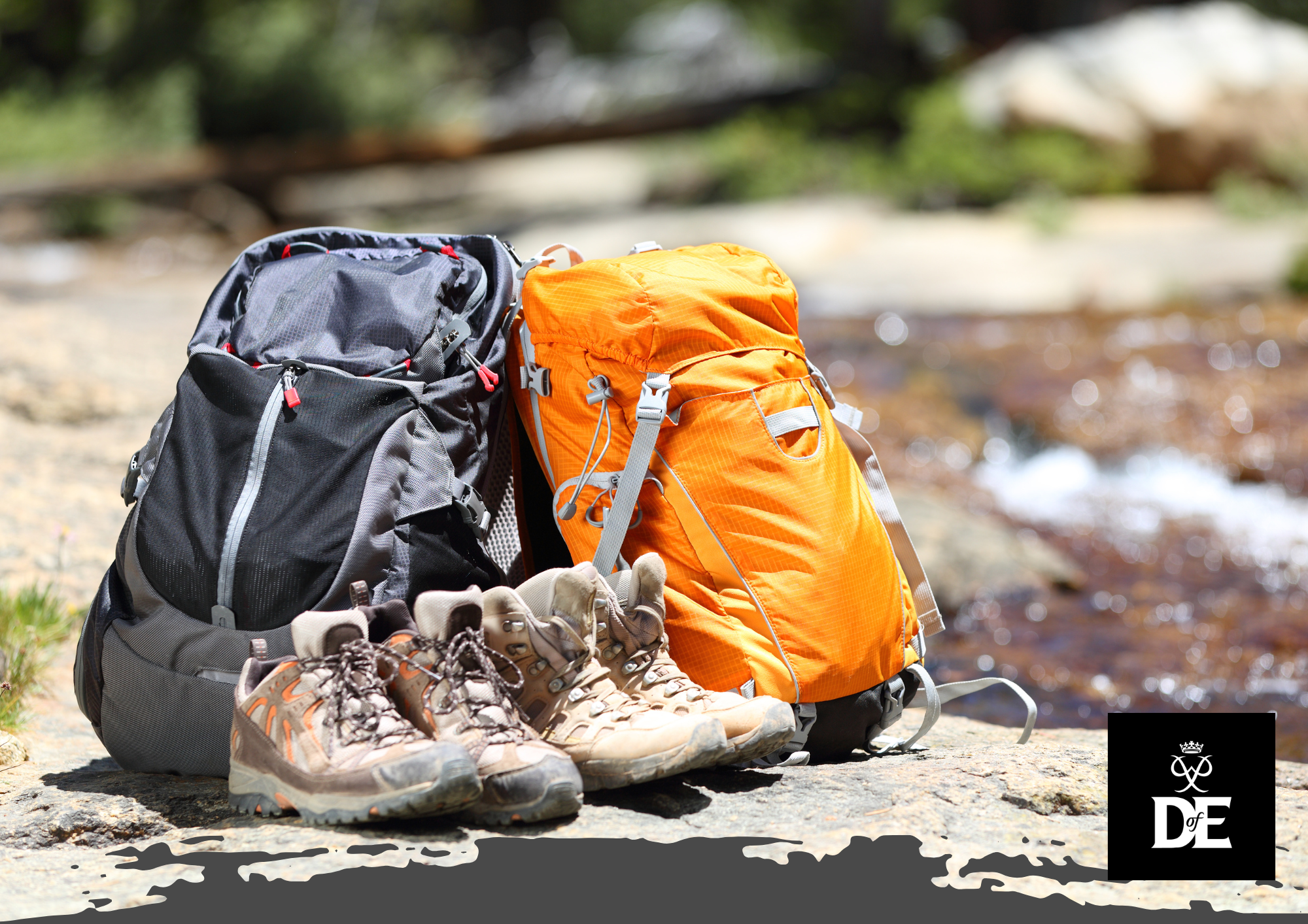 Two hiking backpacks and boots placed on rocky terrain next to a stream, with the Duke of Edinburgh’s Award logo in the corner.