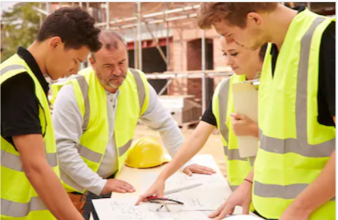 young people in high vis jackets on a building site looking at plans