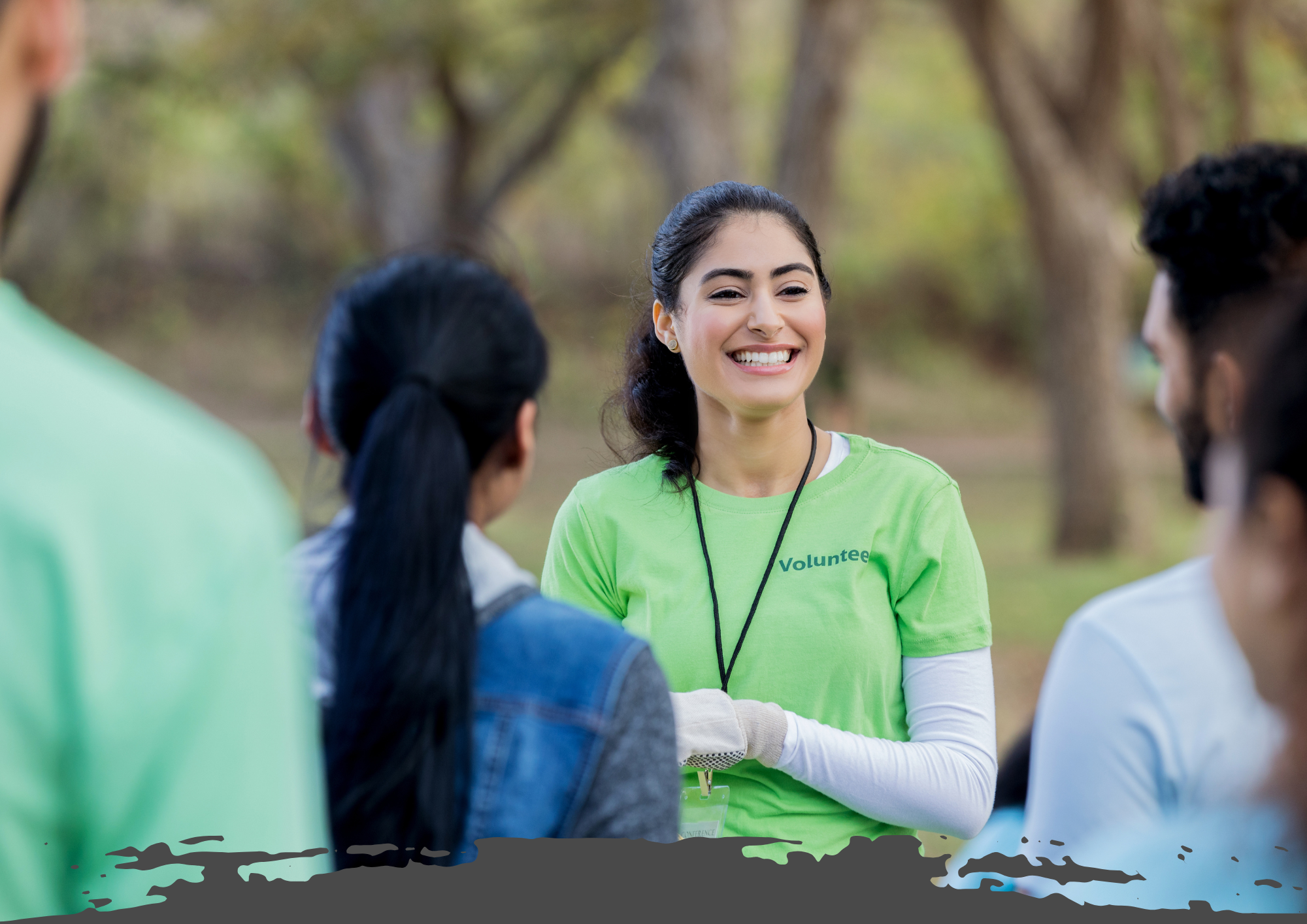 Smiling young volunteer in a green shirt, interacting with a group outdoors during a community event.