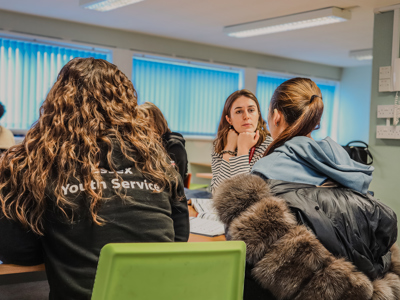 A young women sitting at a table in conversation with a female youth worker, who is attentively listening. Another woman is wearing an ‘Essex Youth Service’ jacket.