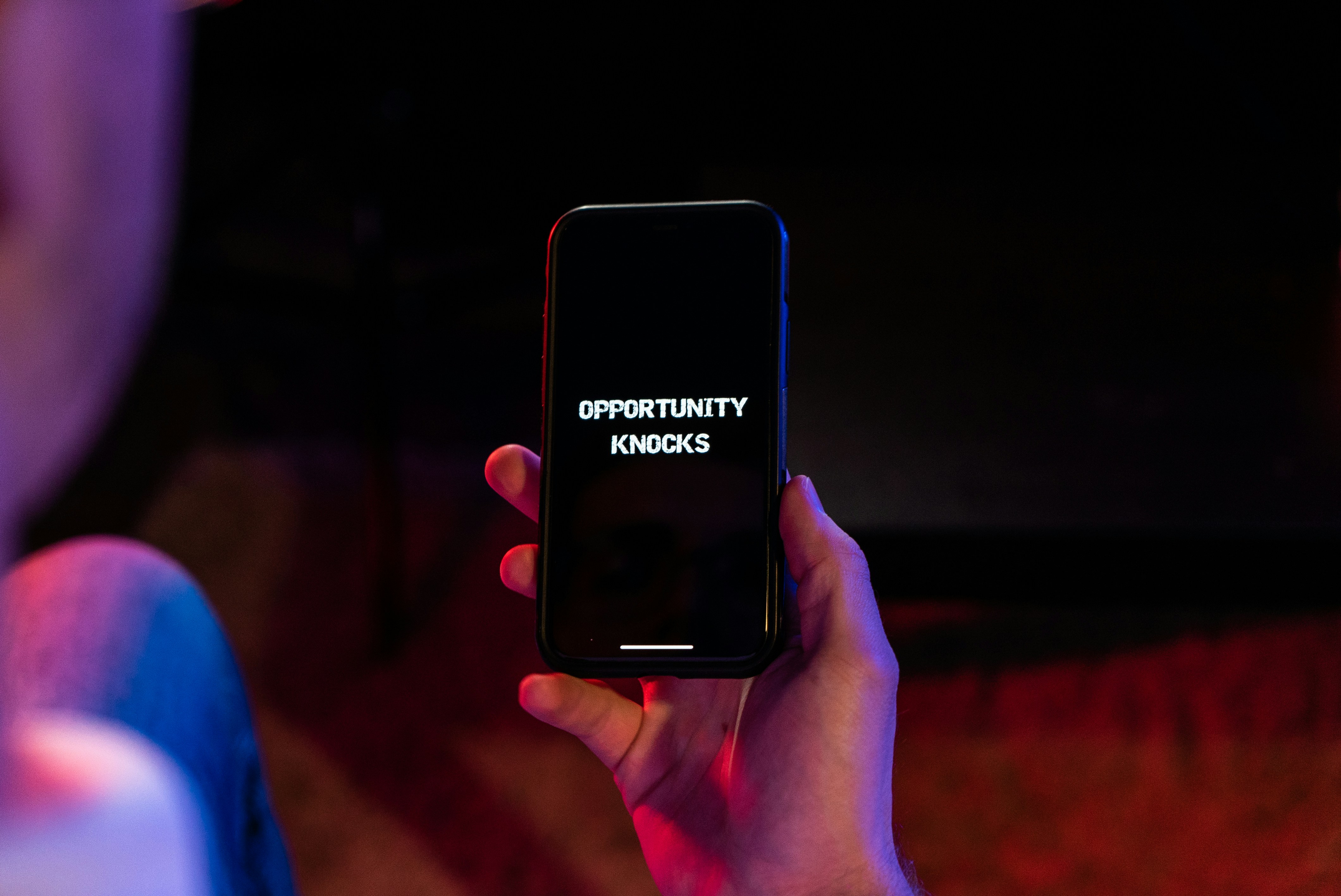 Hand holding a smartphone displaying the text ‘OPPORTUNITY KNOCKS’ on the screen.