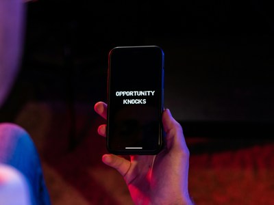 Hand holding a smartphone displaying the text ‘OPPORTUNITY KNOCKS’ on the screen.