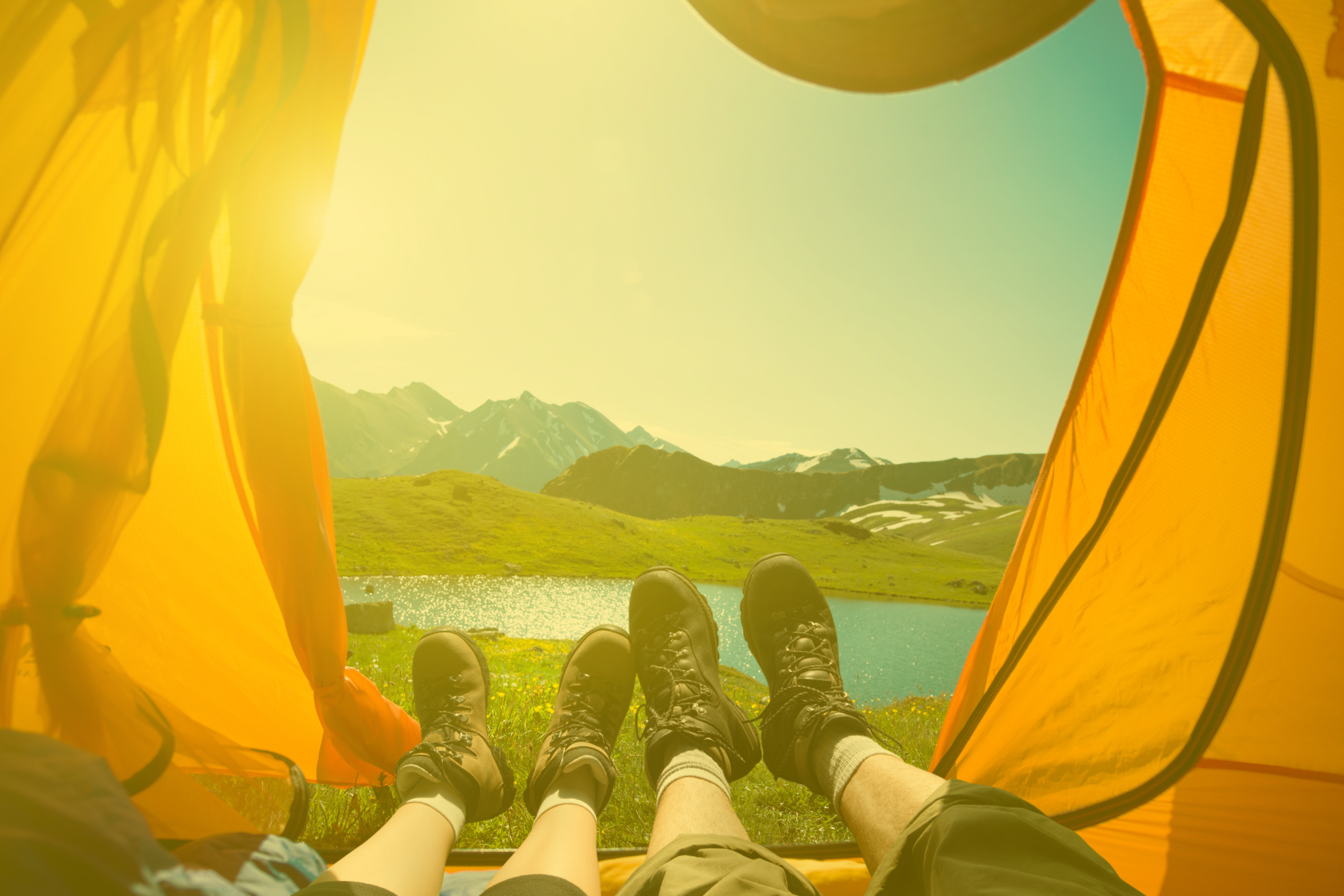 Feet inside a tent overlooking a bright, sunny mountain landscape