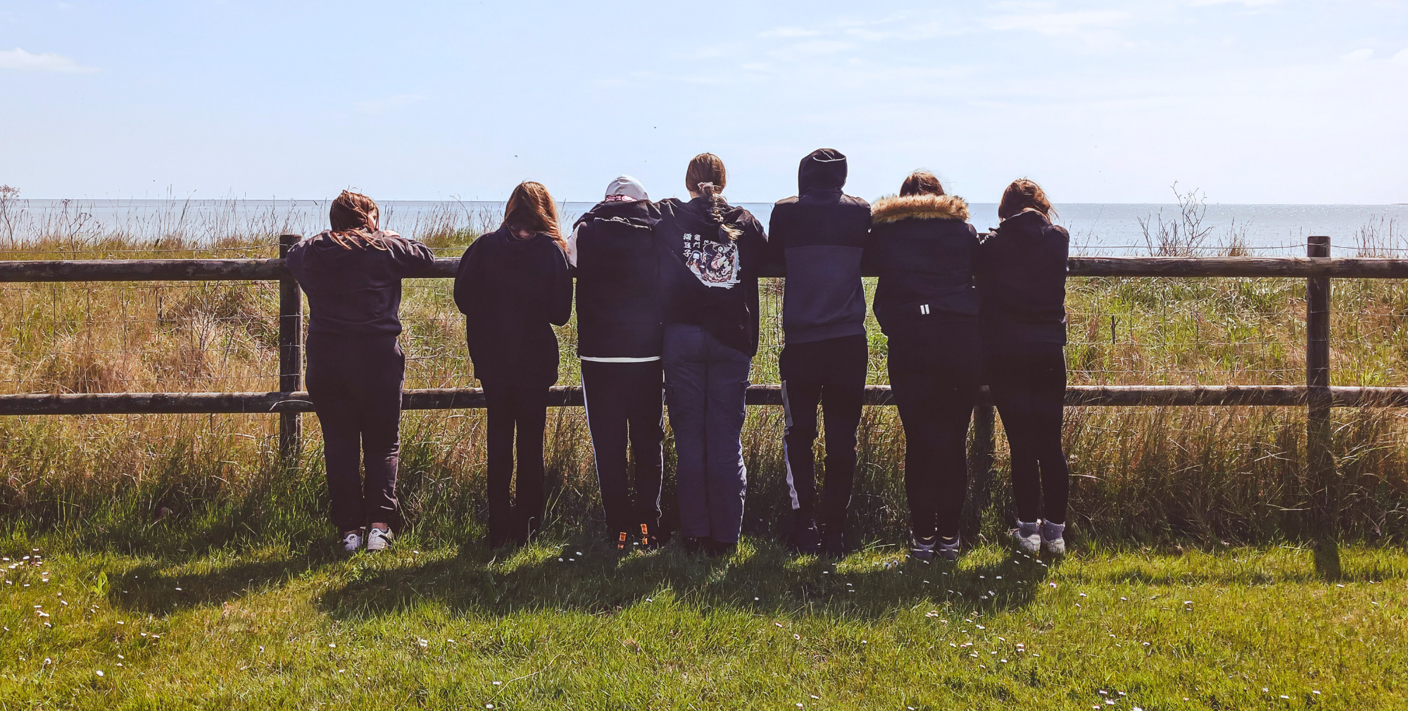 Young people standing by a fence looking out towards the coast during an outdoor visit